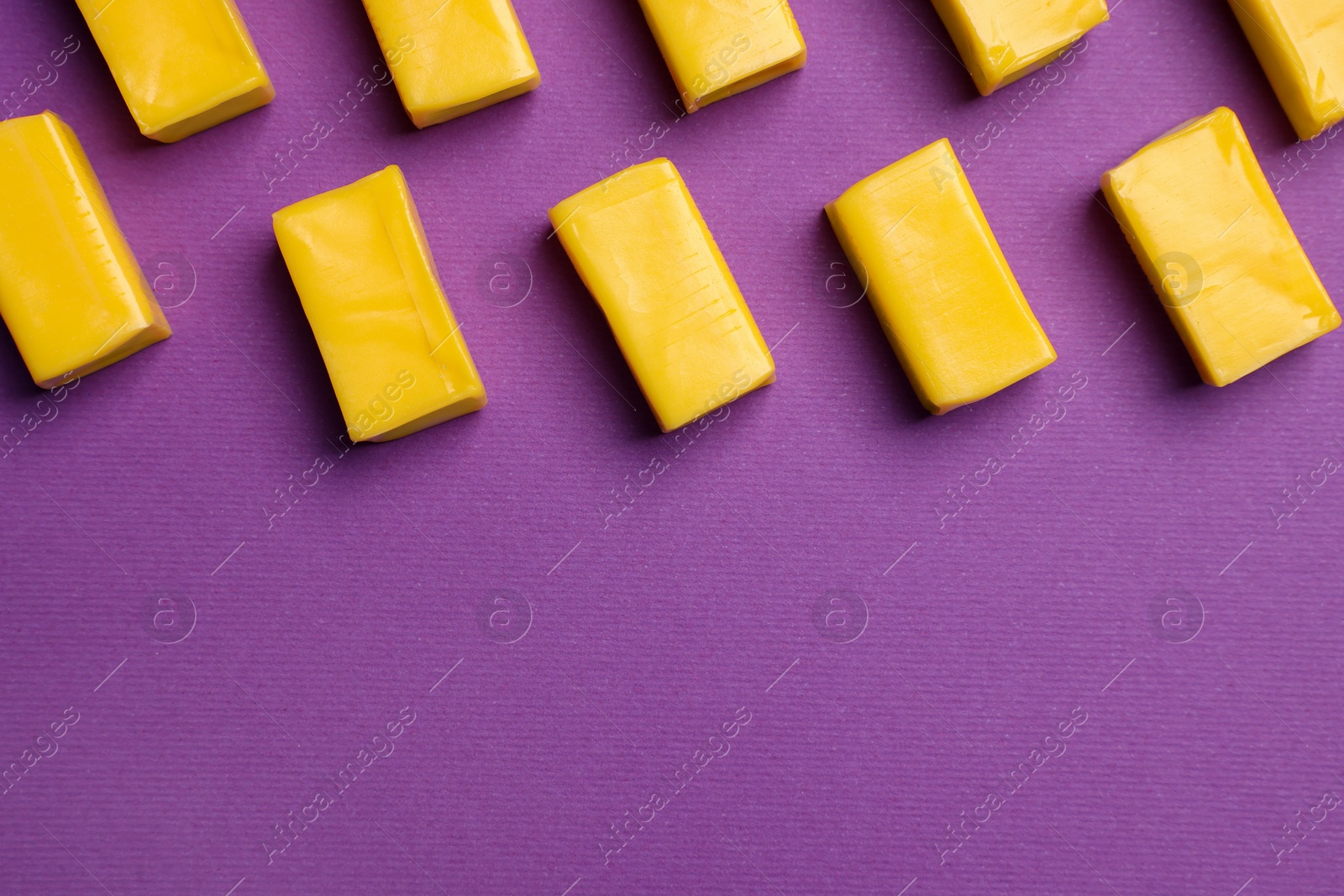 Photo of Yellow bubble gums on purple background, flat lay. Space for text