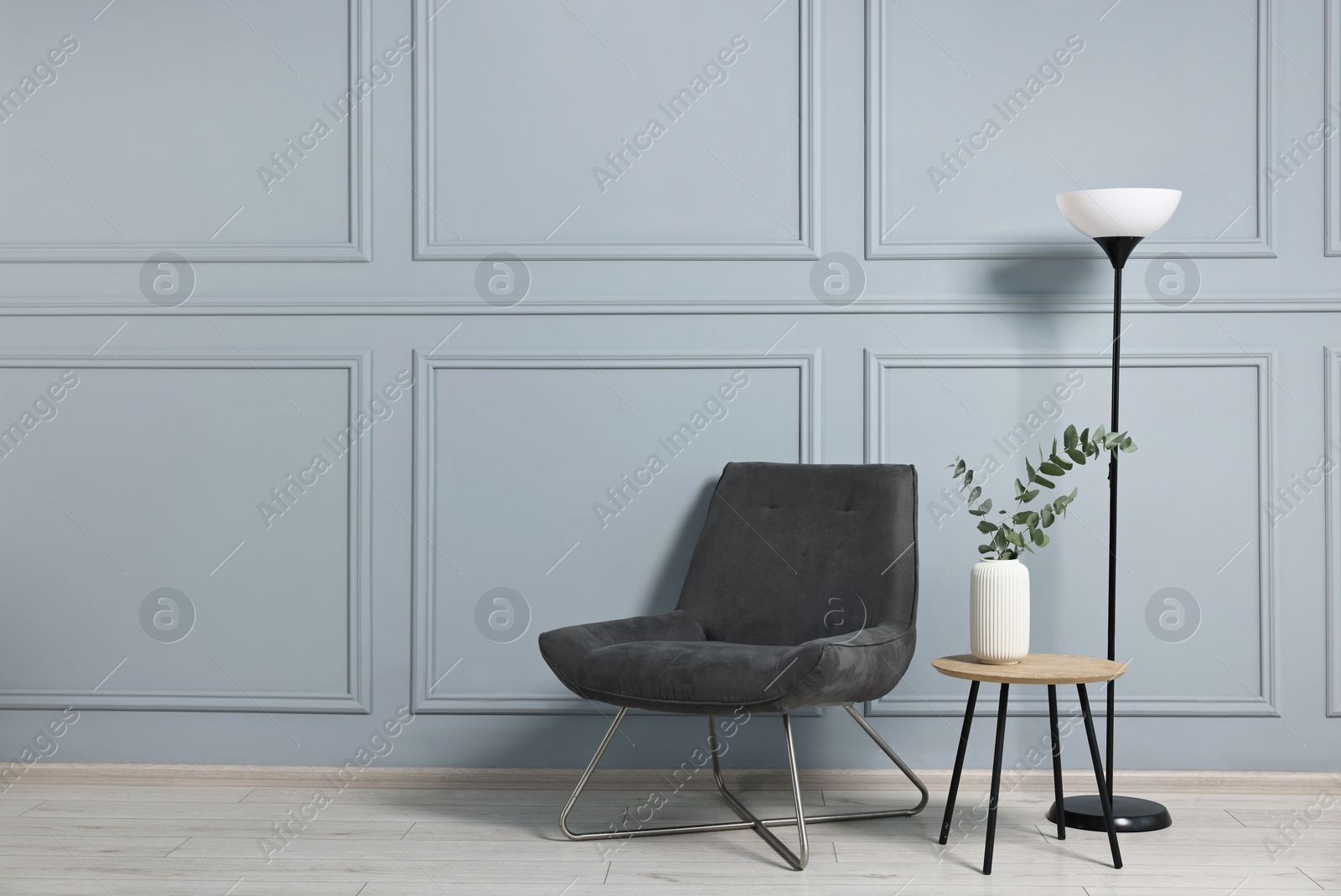 Photo of Comfortable armchair, side table, lamp and eucalyptus indoors, space for text