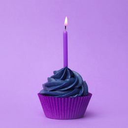 Delicious birthday cupcake with dark blue cream and burning candle on violet background