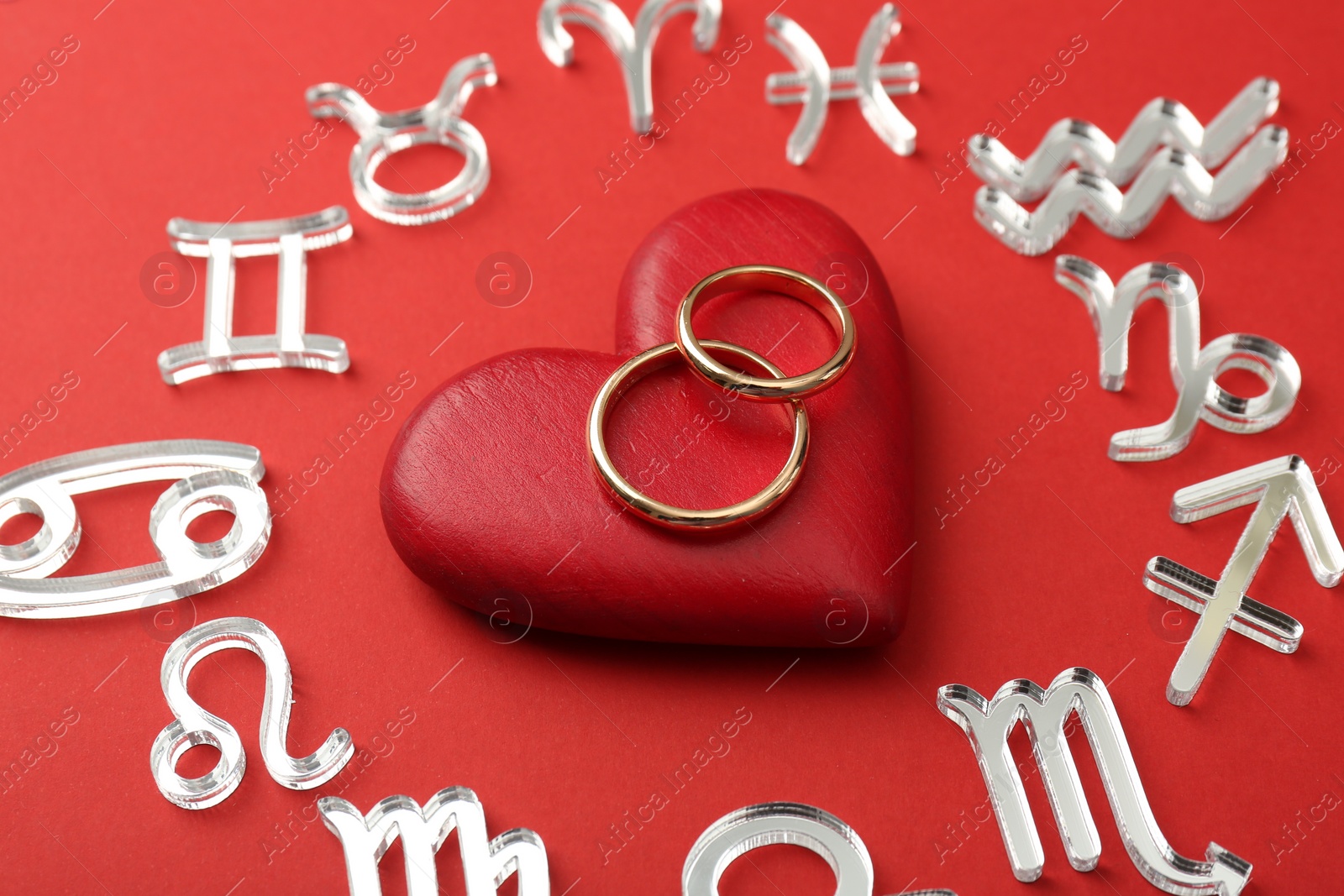 Photo of Zodiac signs, heart and wedding rings on red background