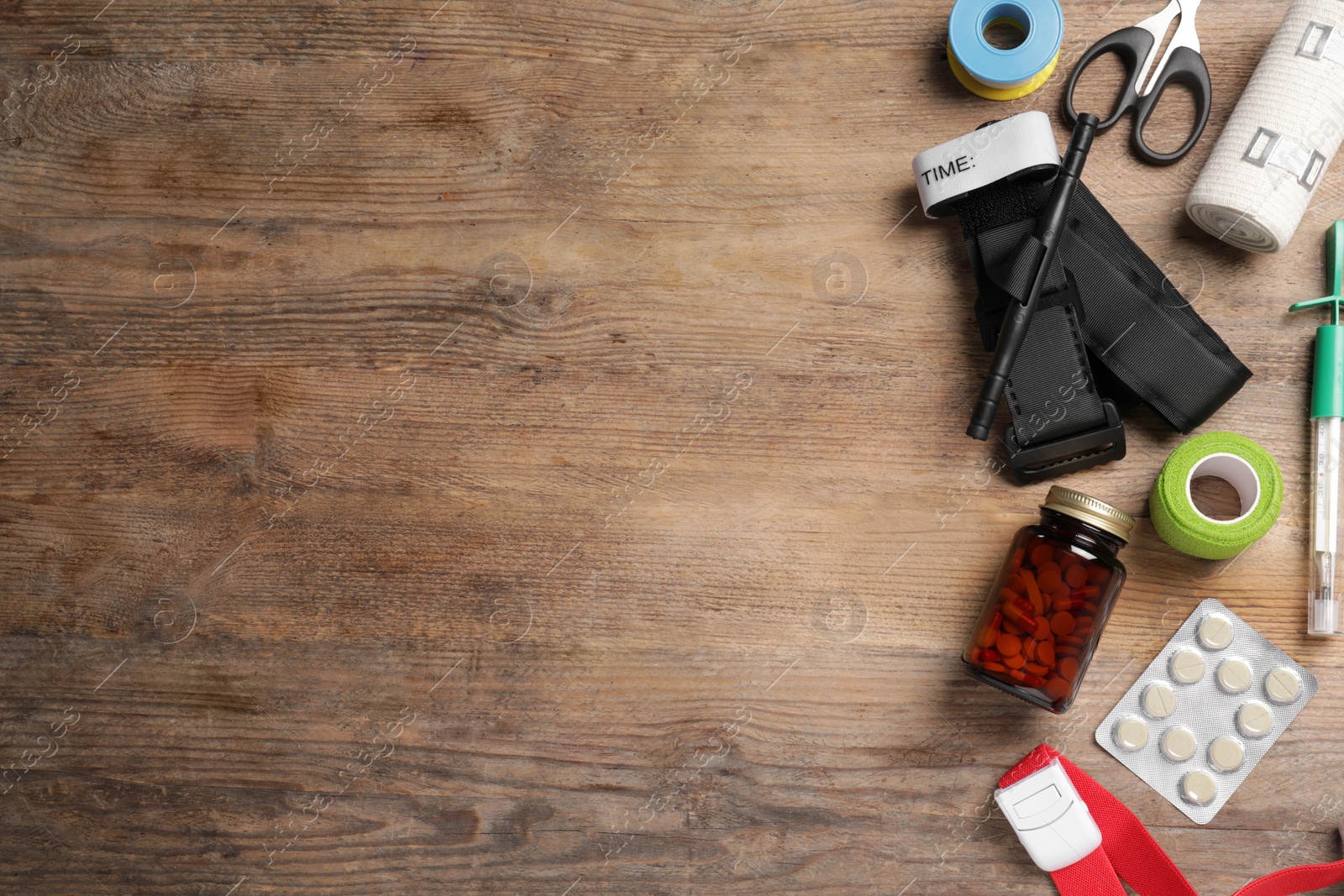 Photo of Tourniquet, elastic bandage, scissors and pills on wooden table, flat lay. Space for text