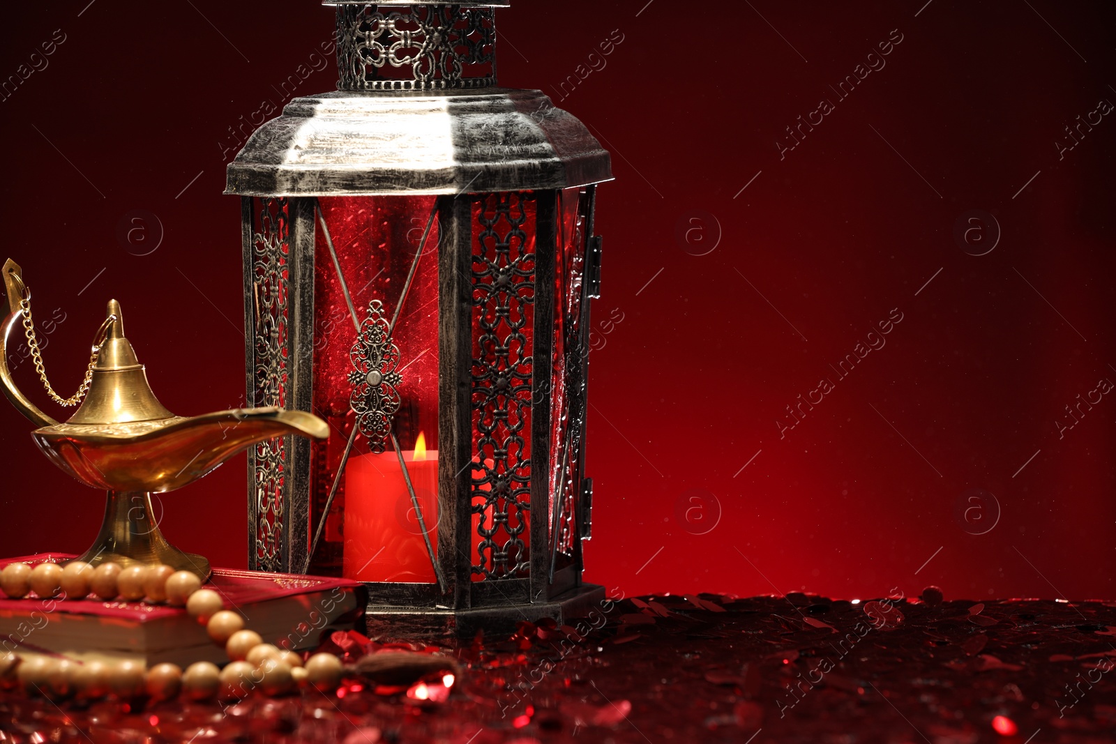 Photo of Arabic lantern, Quran, misbaha and Aladdin magic lamp on shiny red table. Space for text