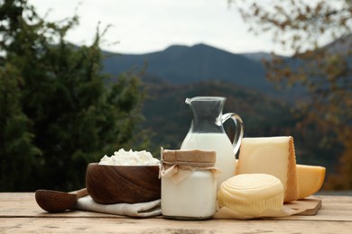 Photo of Tasty cottage cheese and other fresh dairy products on wooden table in mountains