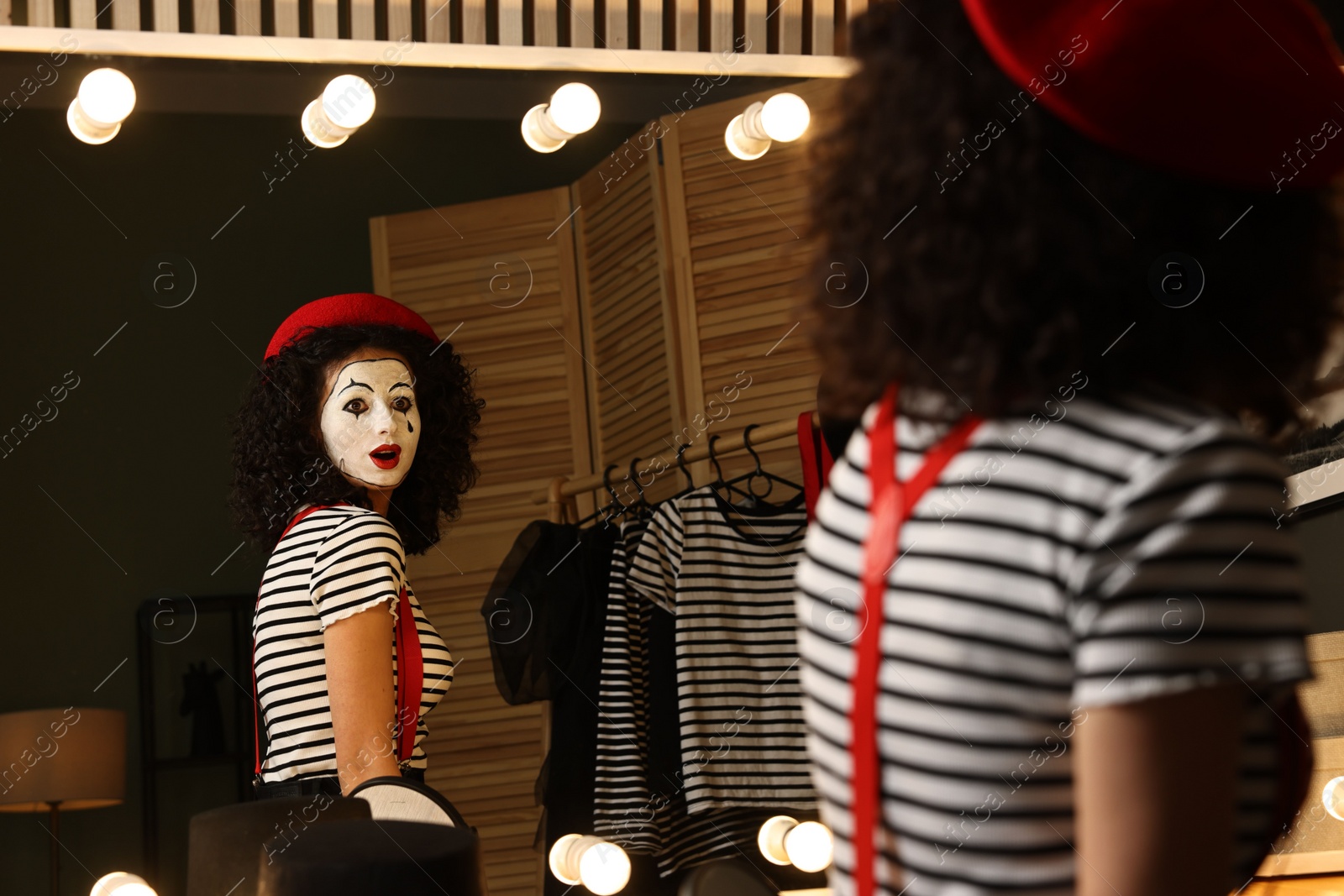 Photo of Young woman in mime costume posing near mirror indoors