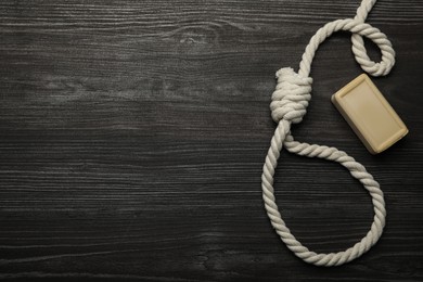 Photo of Rope noose and soap bar on dark wooden table, flat lay. Space for text