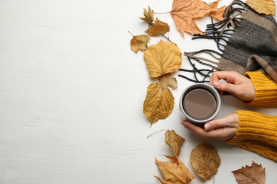 Woman with cup of hot drink at white wooden table, top view with space for text. Cozy autumn atmosphere