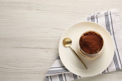 Delicious tiramisu in glass and spoon on white wooden table, top view. Space for text