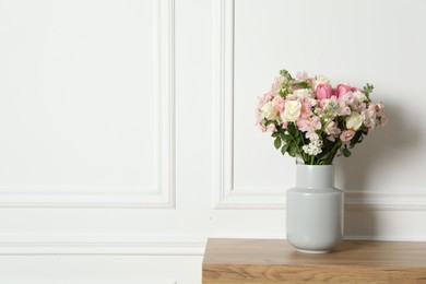 Beautiful bouquet of fresh flowers in vase on wooden table near white wall, space for text