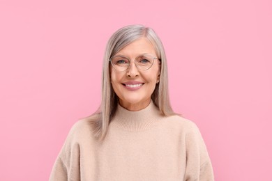 Photo of Portrait of beautiful middle aged woman in eyeglasses on pink background, space for text