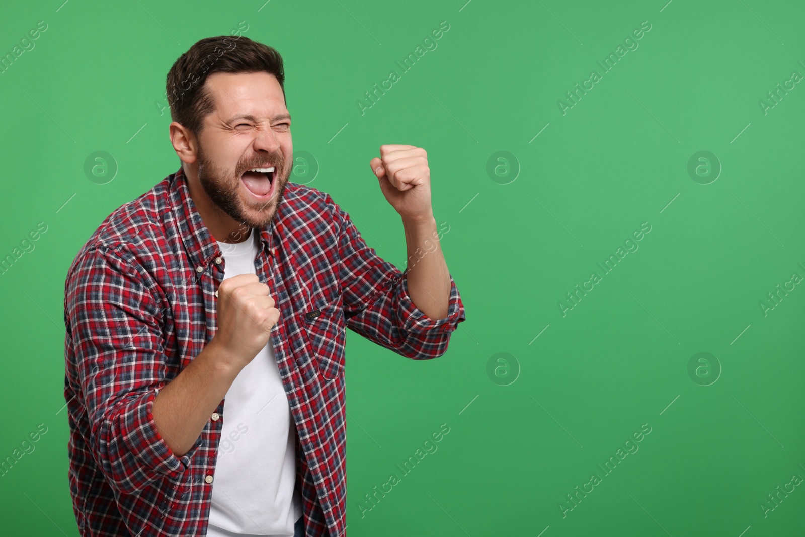 Photo of Emotional sports fan celebrating on green background. Space for text