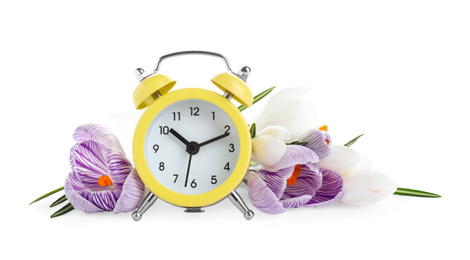 Photo of Yellow alarm clock and spring flowers on white background. Time change