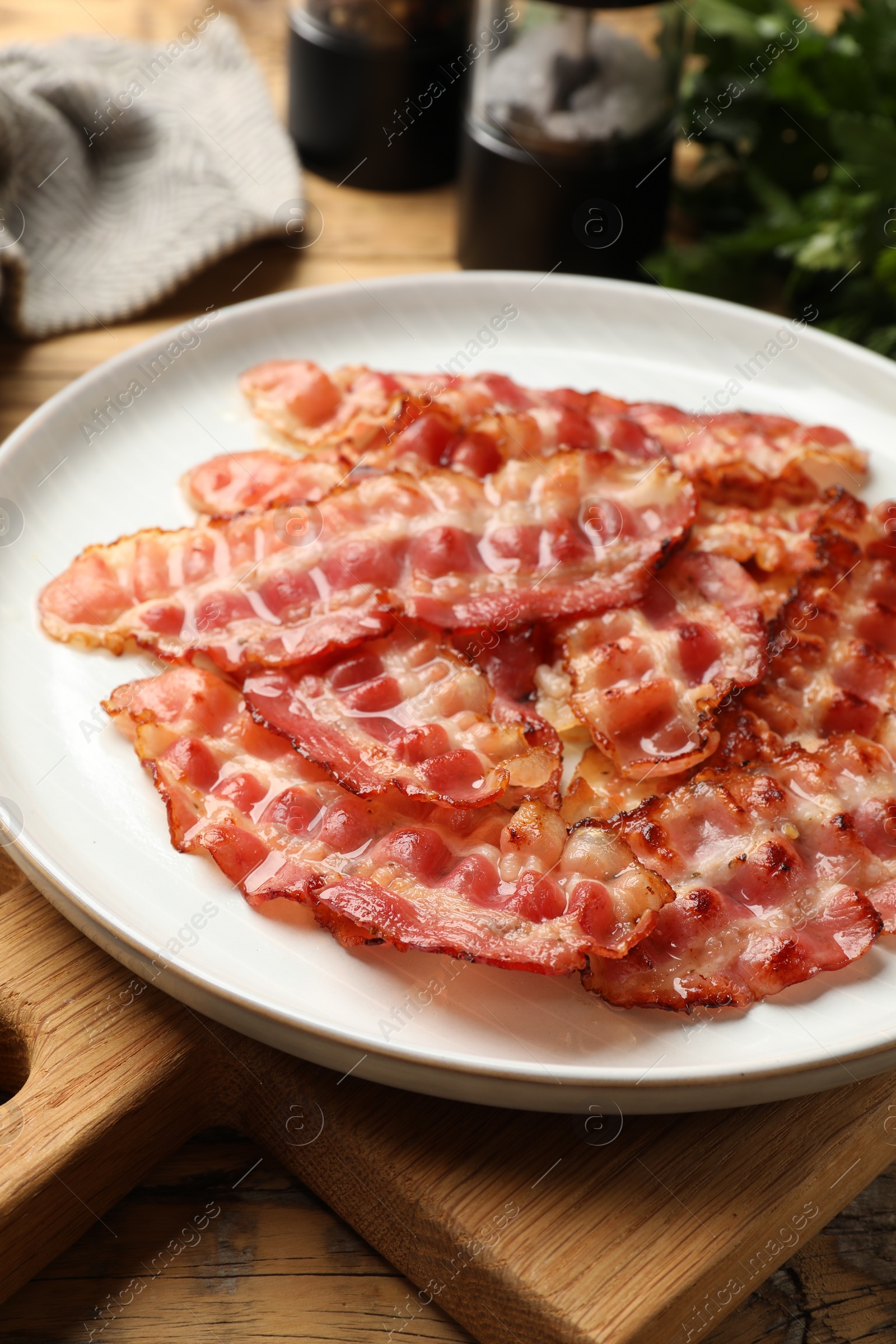 Photo of Plate with fried bacon slices on wooden table, closeup