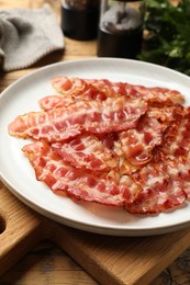 Plate with fried bacon slices on wooden table, closeup
