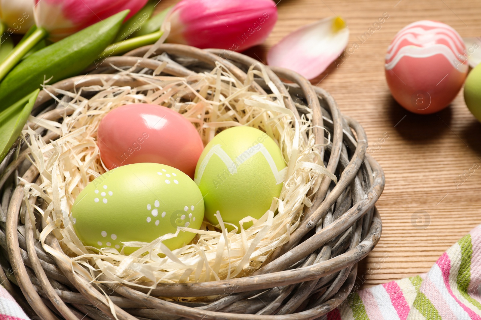 Photo of Wicker nest with painted Easter eggs on wooden table