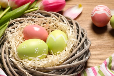 Photo of Wicker nest with painted Easter eggs on wooden table