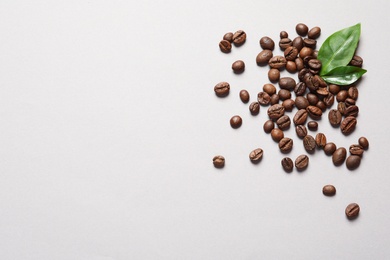 Fresh green coffee leaves and beans on light background, flat lay. Space for text