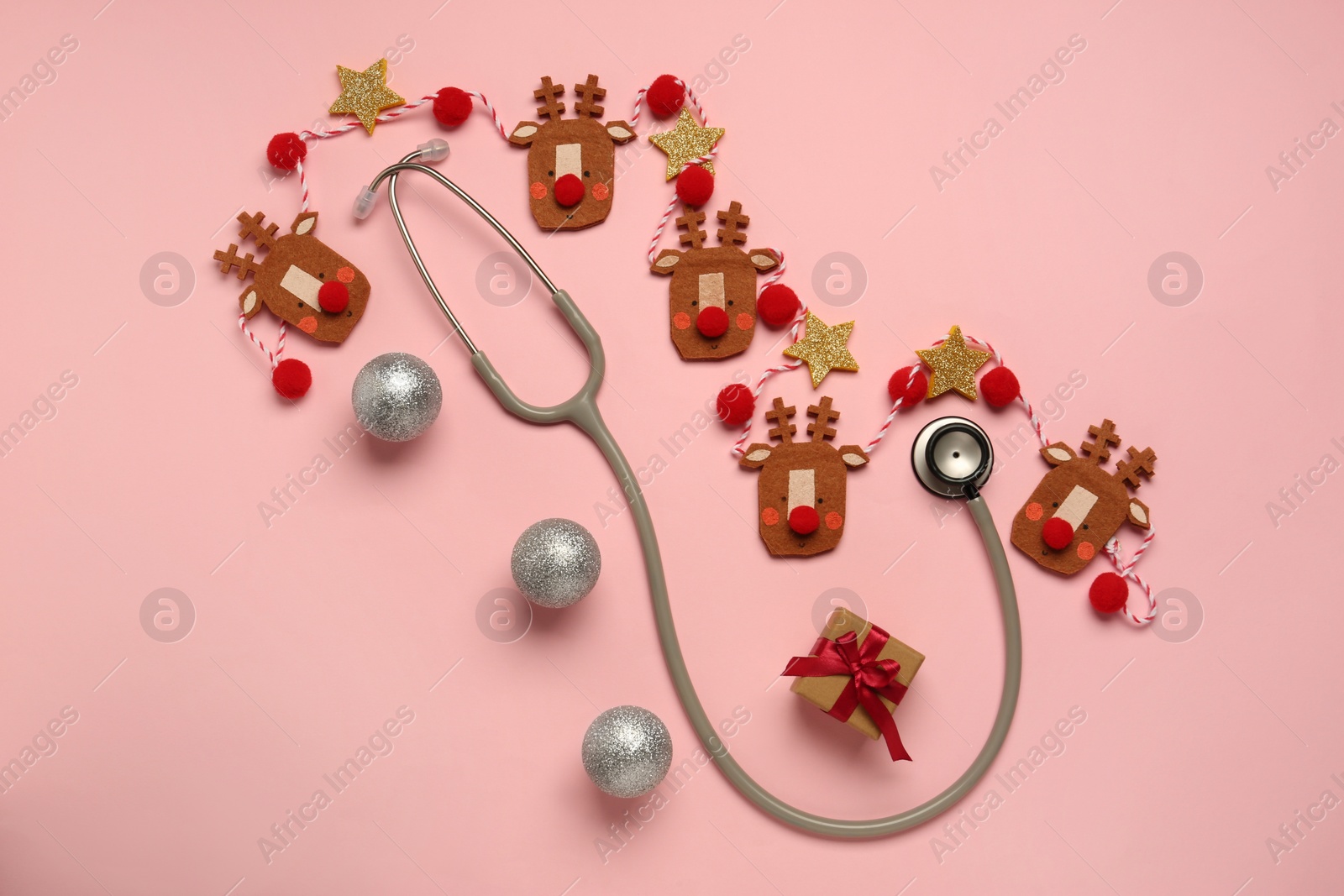 Photo of Greeting card for doctor with stethoscope, gift box and Christmas decor on pink background, flat lay