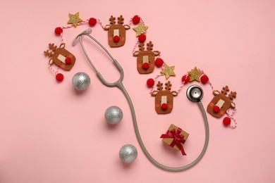 Photo of Greeting card for doctor with stethoscope, gift box and Christmas decor on pink background, flat lay