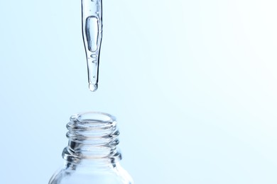 Photo of Dripping liquid from pipette into glass bottle on light blue background, closeup. Space for text