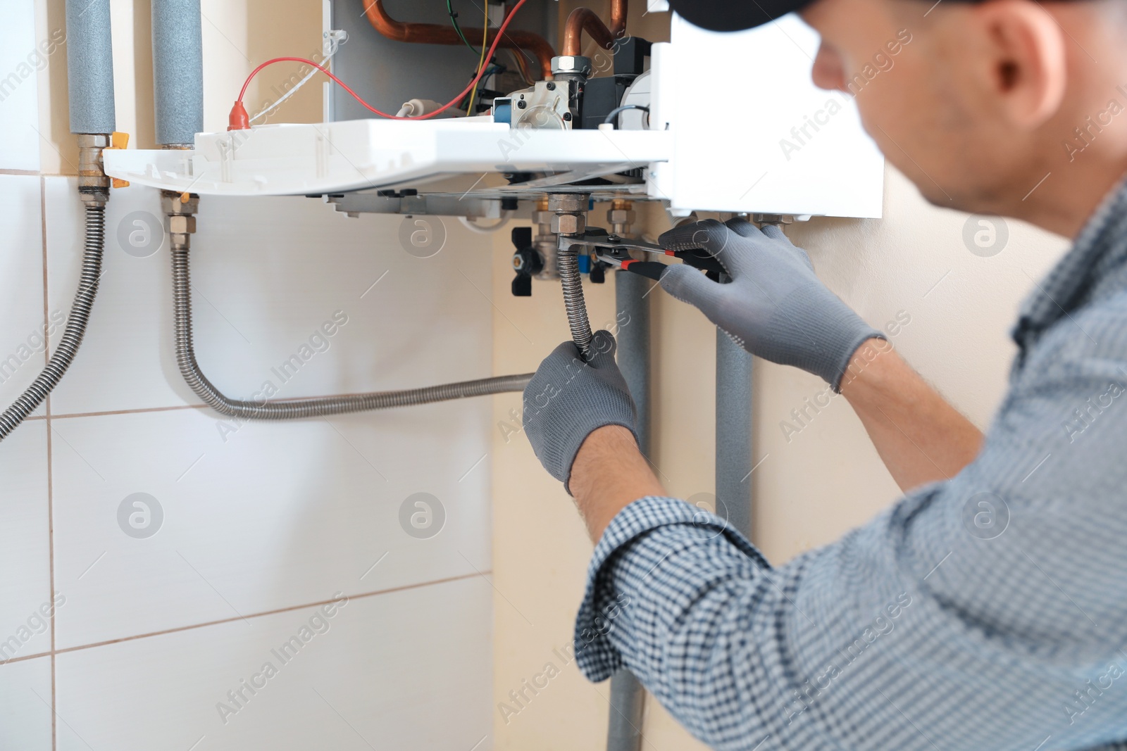 Photo of Man repairing gas boiler with waterpump plier indoors, closeup