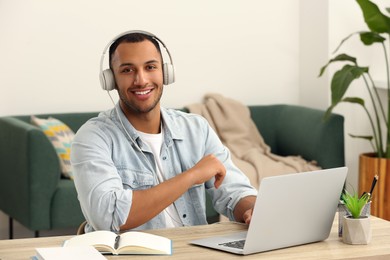 Photo of Portrait of African American man in headphones near laptop at wooden table in room