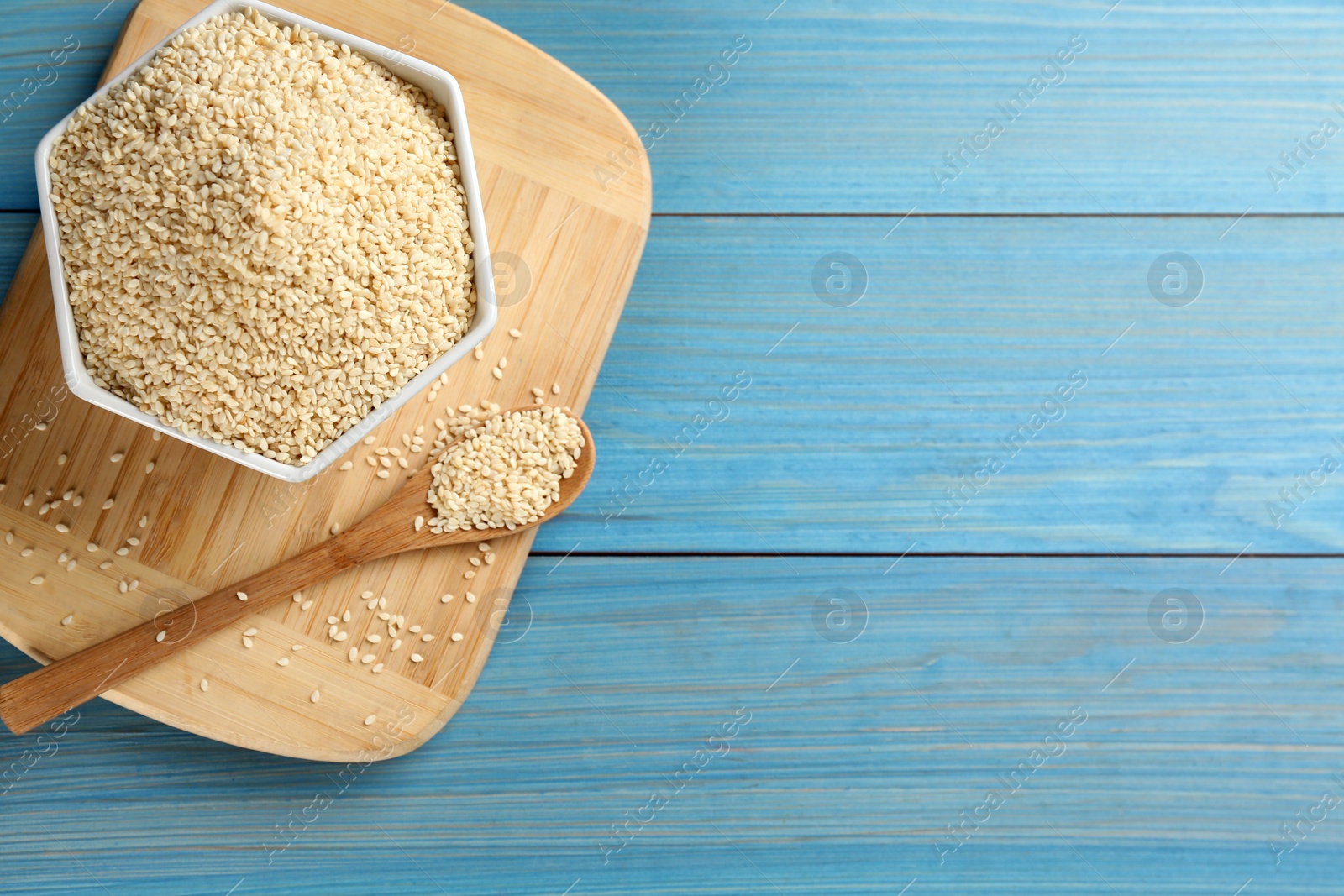 Photo of White sesame seeds on light blue wooden table, flat lay. Space for text