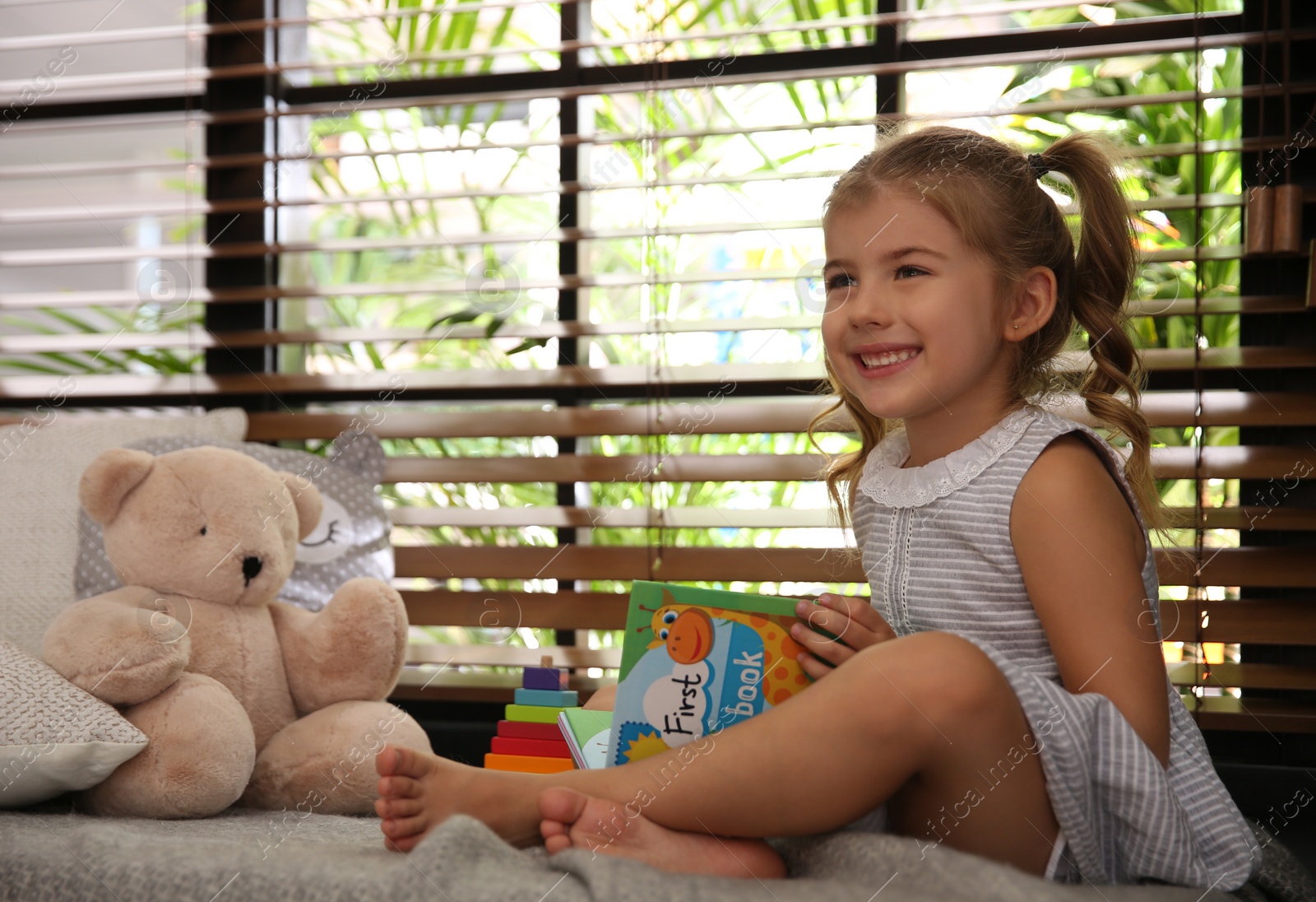 Photo of Cute little girl playing near window at home