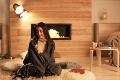 Photo of Young woman resting near decorative fireplace at home. Winter season