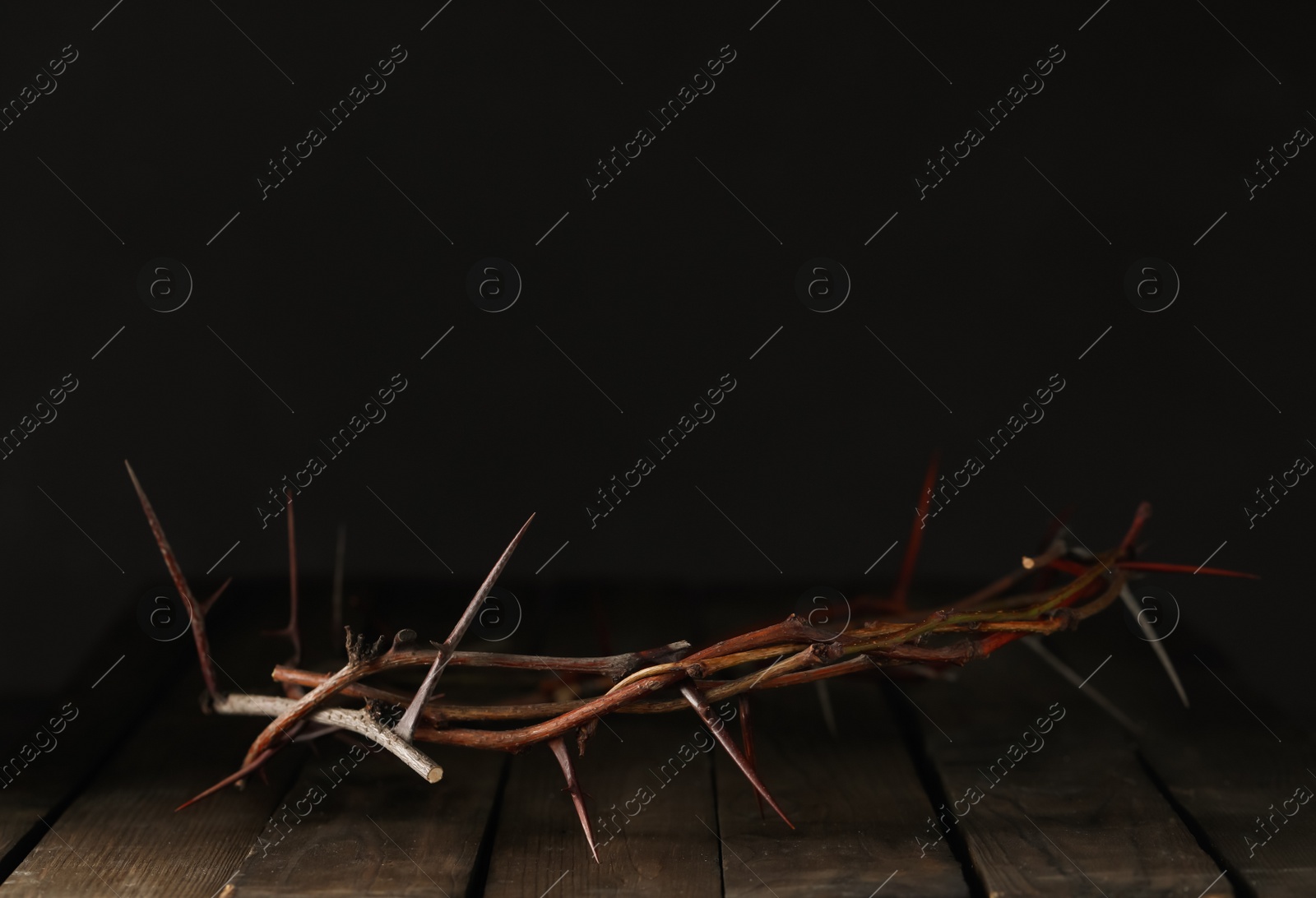 Photo of Crown of thorns on wooden table against dark background, space for text. Easter attribute