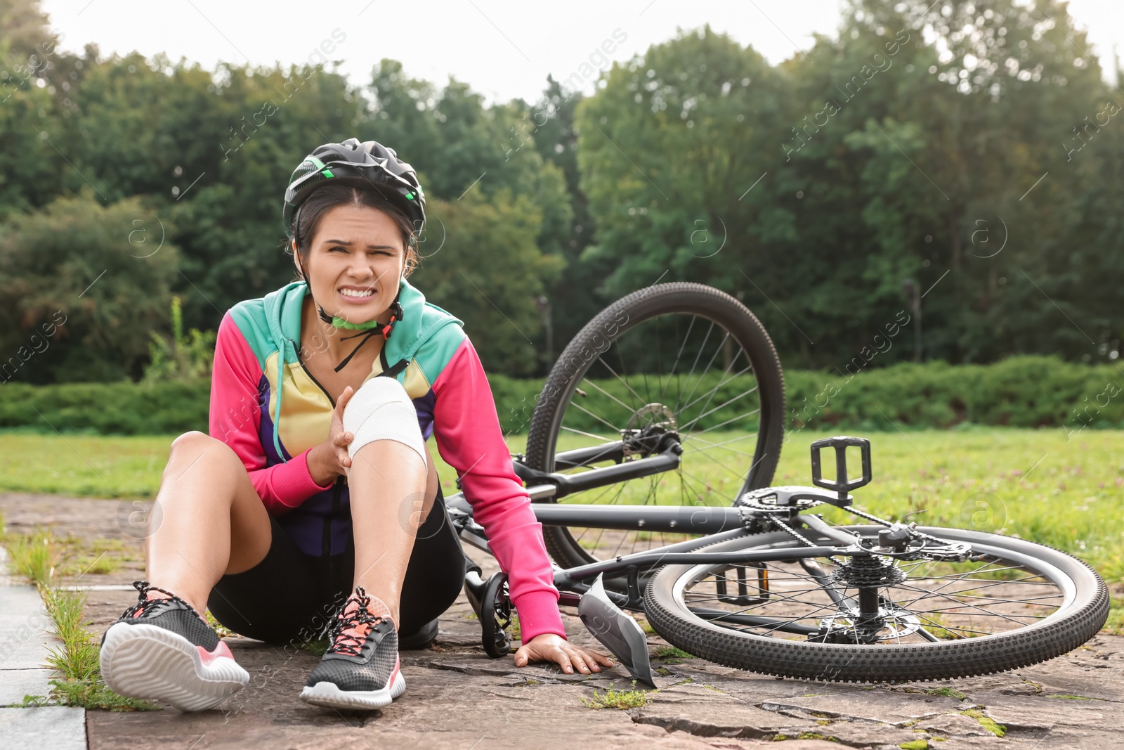 Photo of Young woman with injured knee near bicycle outdoors