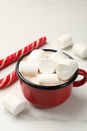 Photo of Tasty hot chocolate with marshmallows and candy cane on white marble table, closeup