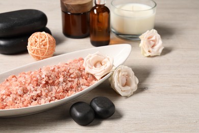 Photo of Natural sea salt in bowl and other spa supplies on wooden table