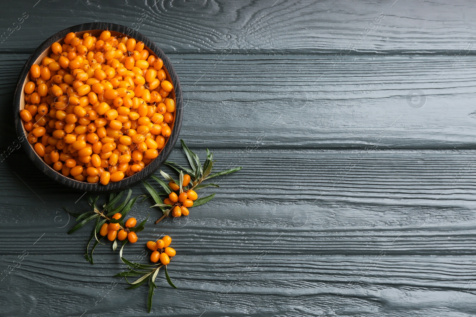 Photo of Ripe sea buckthorn berries on grey wooden table, flat lay. Space for text