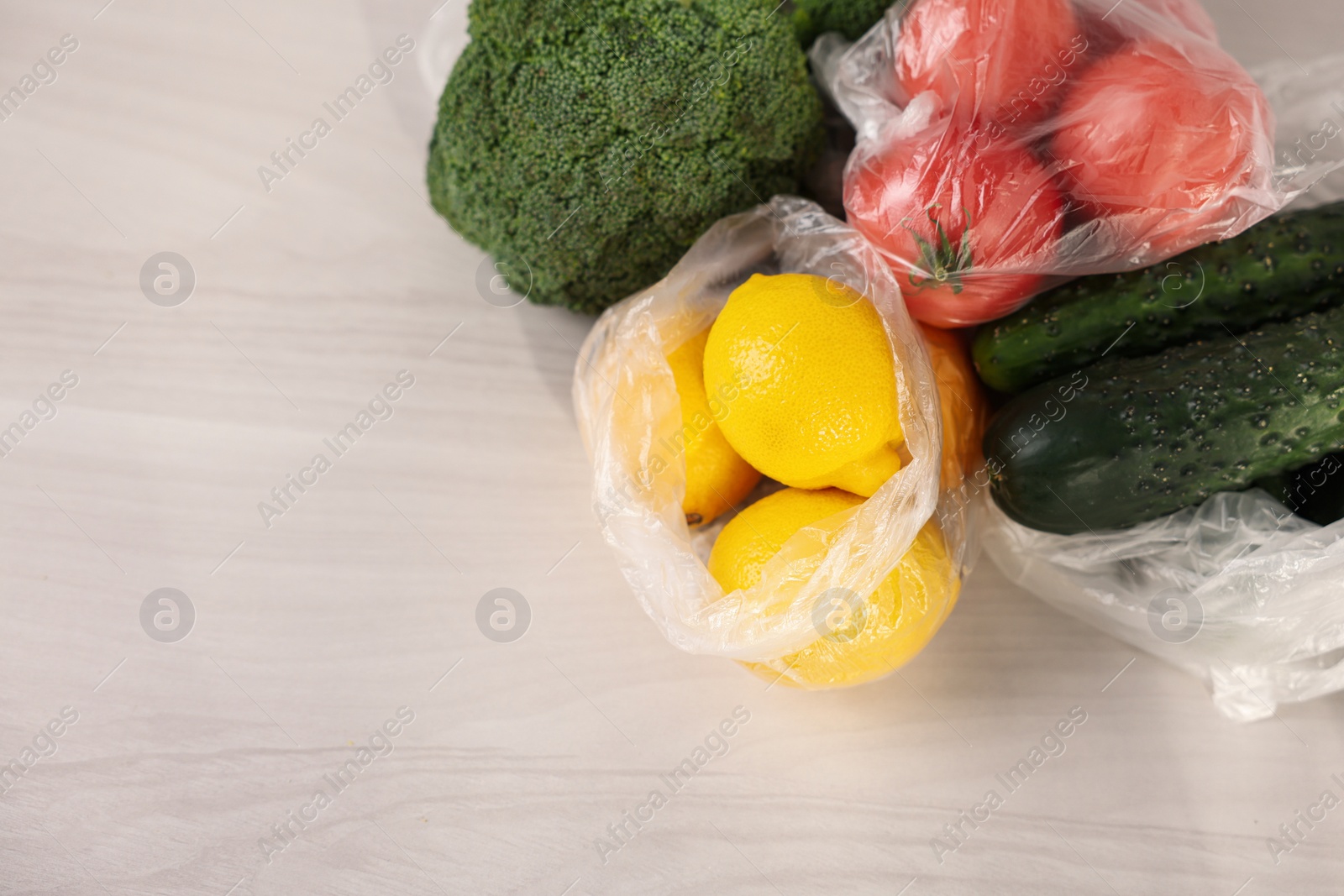 Photo of Plastic bags and fresh products on white table, flat lay. Space for text