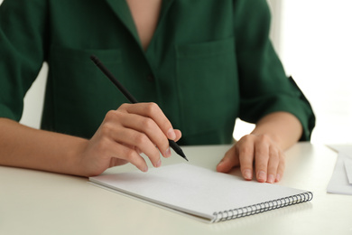 Photo of Woman drawing with pencil in notepad at white table, closeup