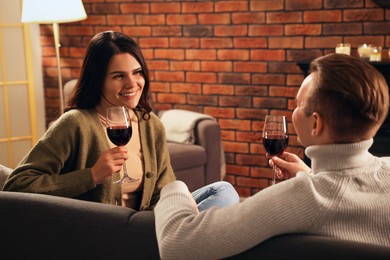 Photo of Happy lovely couple with glasses of wine spending time together near fireplace at home