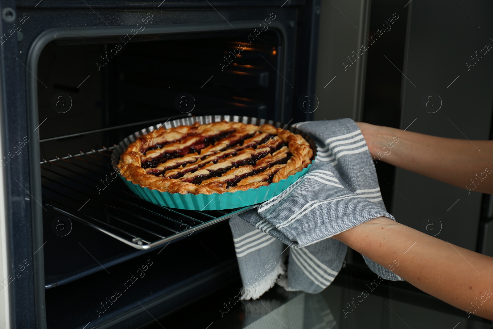 Photo of Woman taking delicious fresh homemade cake out of oven indoors, closeup