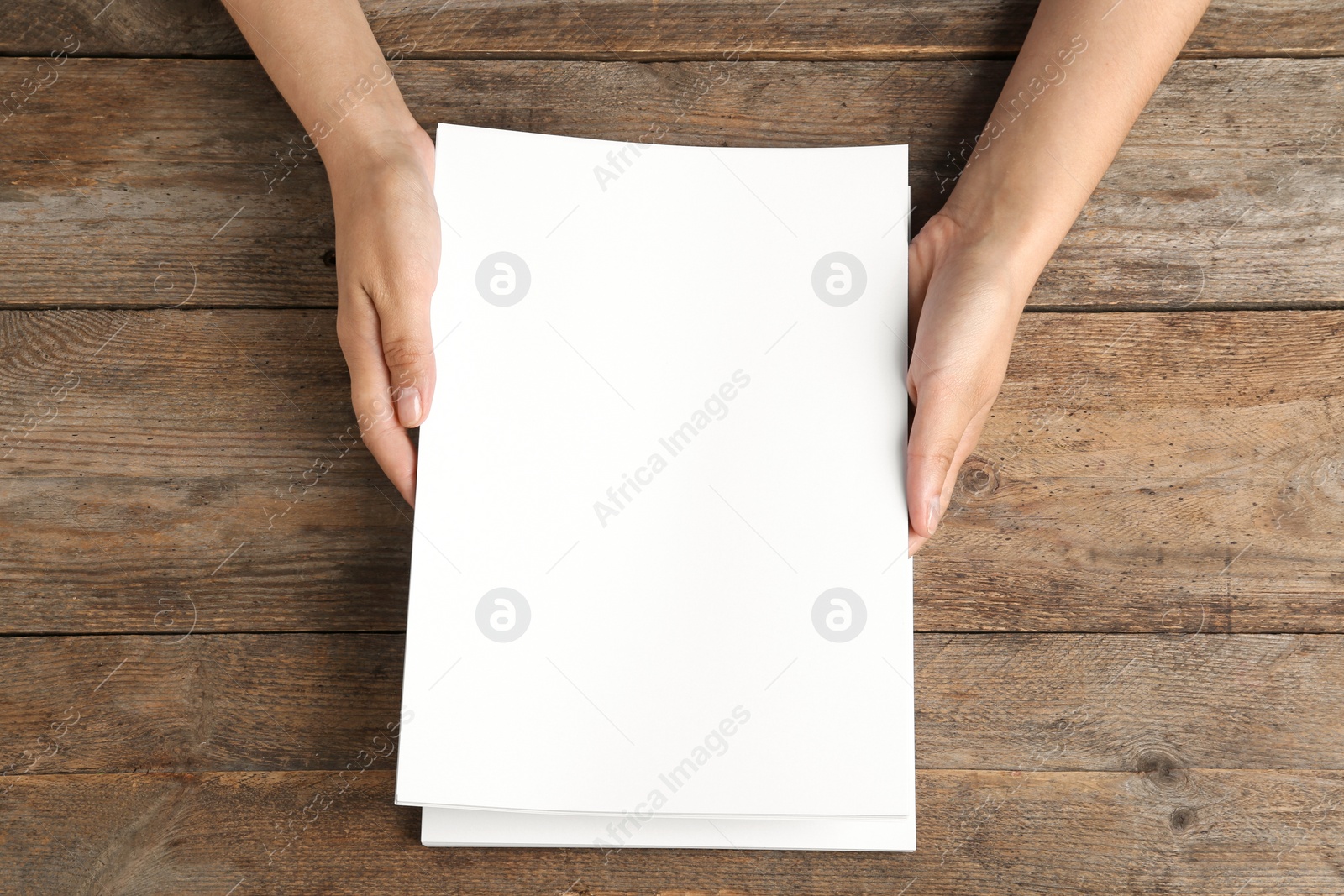 Photo of Woman holding blank paper sheets for brochure at wooden table, top view. Mock up