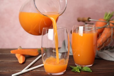 Photo of Pouring freshly made carrot juice into glass on wooden table