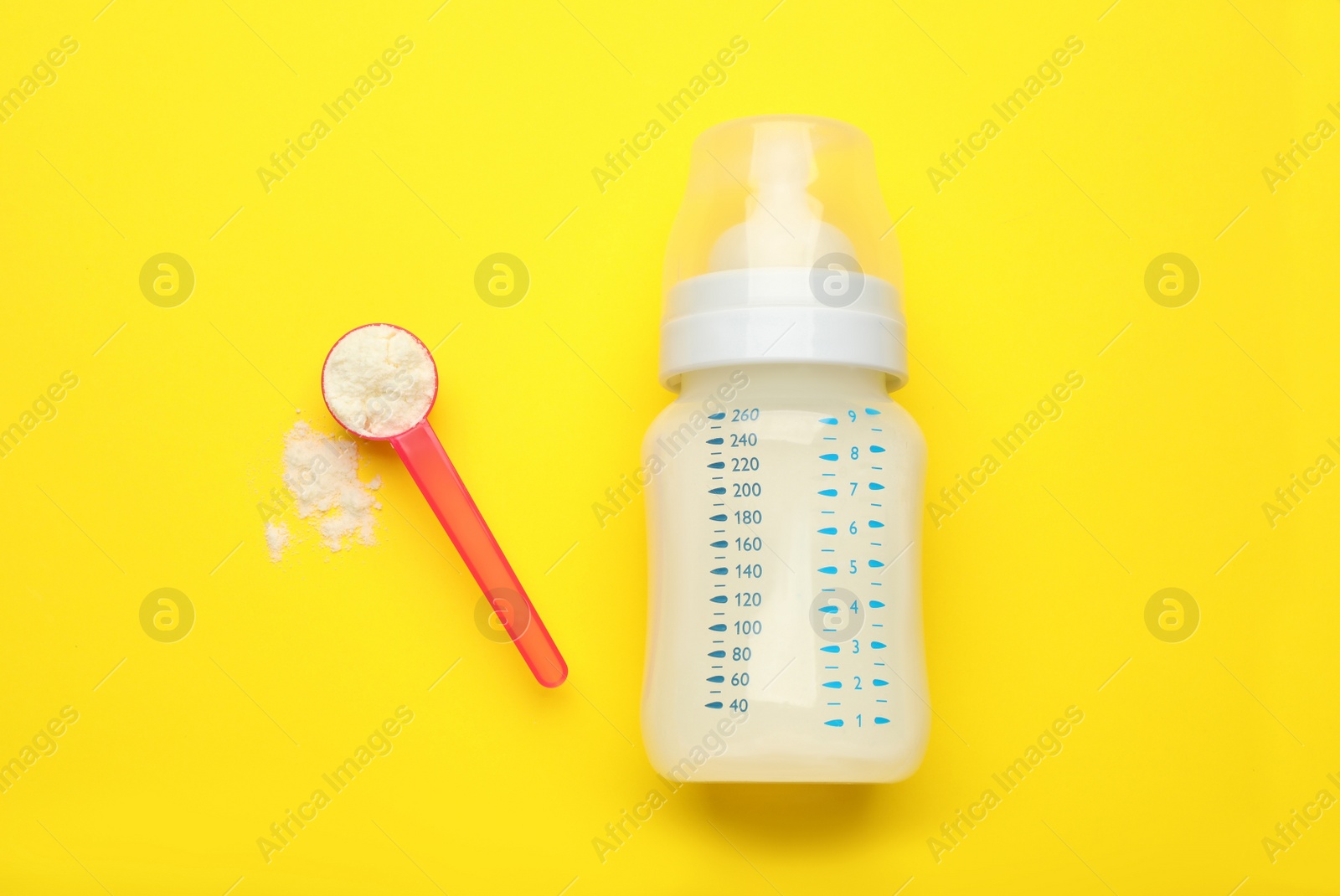 Photo of Feeding bottle with infant formula and powder on yellow background, flat lay