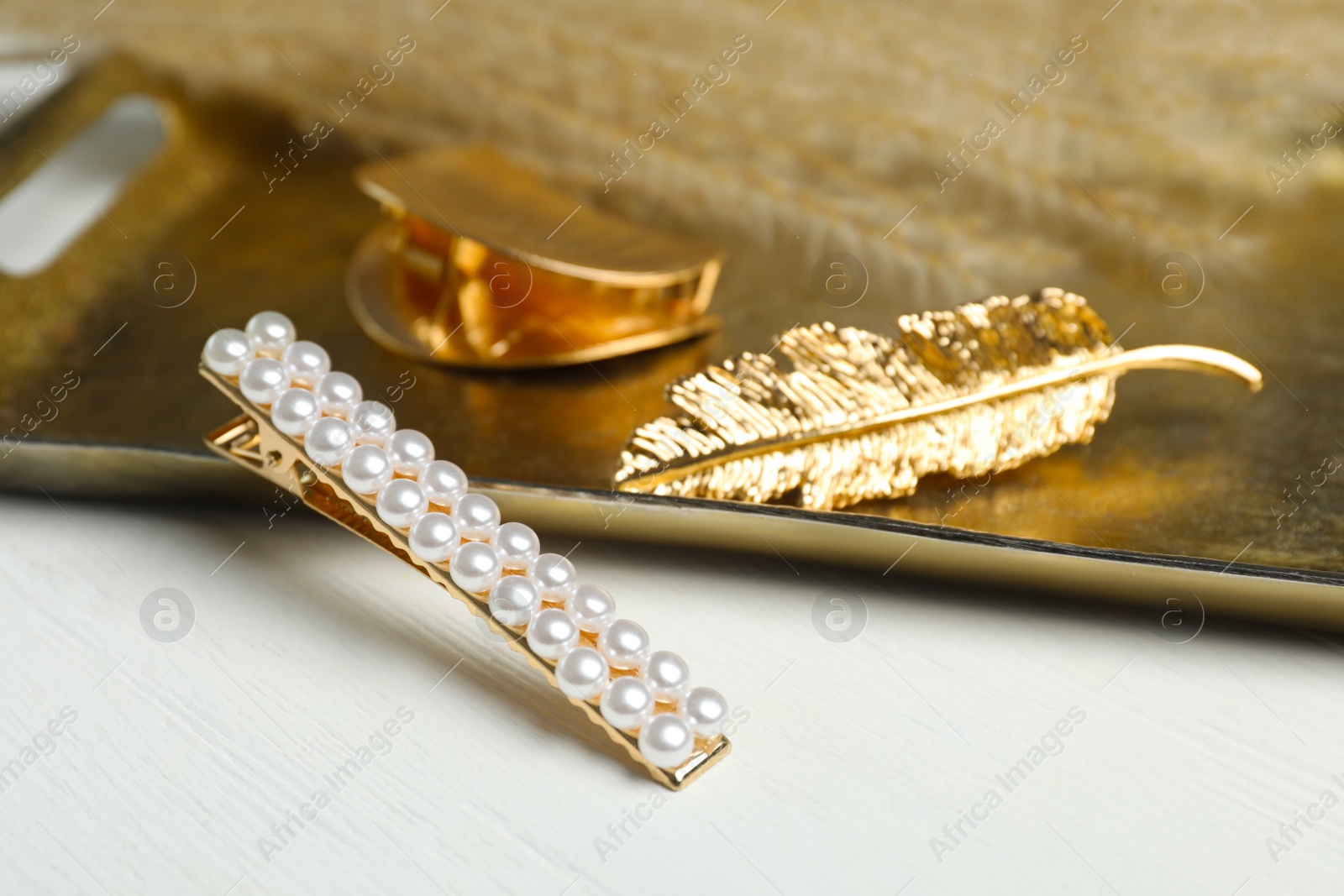 Photo of Stylish hair clips and gold tray on white wooden table