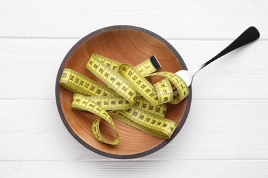 Photo of Bowl with measuring tape and fork on white wooden table, flat lay. Weight loss concept