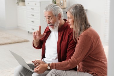 Photo of Senior couple using laptop on sofa at home