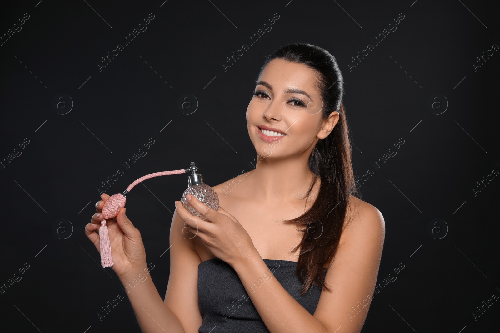 Photo of Young woman with bottle of perfume on black background