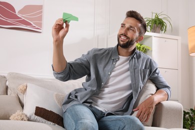 Handsome man playing with paper plane in living room at home