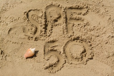 Photo of Abbreviation SPF 50 written on sand and seashell at beach, top view