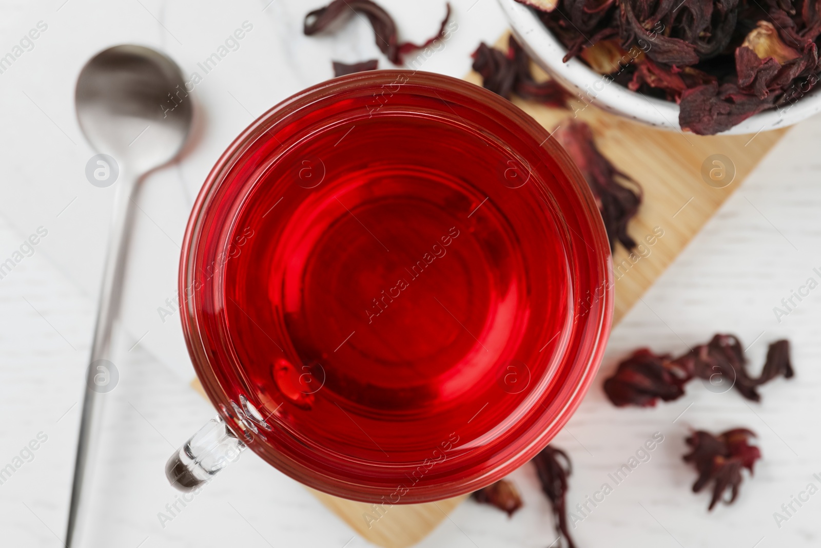 Photo of Cup of fresh hibiscus tea and dry flower leaves on wooden table, flat lay