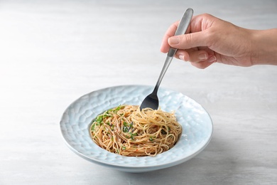 Photo of Woman eating tasty noodles with herbs at table, closeup