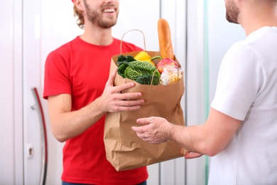 Photo of Courier giving paper bag with products to customer at home, closeup. Food delivery service