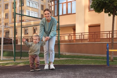 Happy nanny walking with cute little boy outdoors, space for text